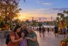 A family checks a phone while walking through a generic Central Florida theme-park promenade at sunset.