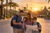 AI-generated editorial image of a family reviewing a phone and blank park map on a generic Central Florida theme-park promenade at sunrise.