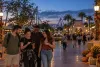 Illustration of visitors checking evening plans on a fall-decorated Central Florida theme-park promenade