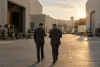 Two corporate attorneys walk through an unbranded Los Angeles film studio lot during merger negotiations.