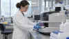 A cardiovascular laboratory researcher handles blood samples beside an unbranded analyzer