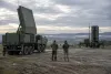 Two technicians stand between an unbranded mobile radar and defensive interceptor launcher on a European training range.