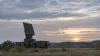A ground-based air-surveillance radar scans the sky over a flat northern European field at dawn.