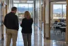 Two school staff members review a clipboard in a quiet public school corridor beside an empty classroom.