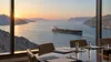 An oil tanker passes through a narrow Gulf waterway beyond an empty conference table at dawn.