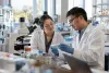 Two university biomedical researchers examine a sample tray together in a naturally lit laboratory.