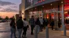 Moviegoers line up outside a contemporary multiplex at dusk.
