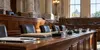 An empty statehouse committee hearing room with microphones and document folders on a polished wood table.