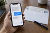 A smartphone displaying abstract message bubbles beside an unmarked ballot envelope and pen.