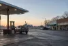 A pickup truck at an unbranded fuel pump beside a rural American main street at dawn