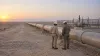 Two civilian inspectors beside an oil pipeline crossing an arid desert landscape at dawn