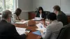 Five anonymous finance and public-administration professionals review charts around an unbranded conference table in natural daylight