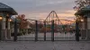 Locked generic amusement park gates with an empty midway and roller coaster silhouette at autumn dusk