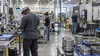 Workers inspect metal components on the floor of a modern manufacturing facility.