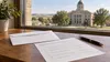 An unmarked ballot, envelope and pen on a wooden table near a county courthouse
