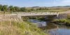 A concrete rural bridge over a prairie creek with survey equipment beside the road in South Dakota
