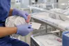 A healthcare worker holds a newborn’s foot beside a blood-spot screening card in a hospital nursery.
