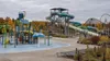 An empty outdoor waterpark with colorful slides and a family splash area surrounded by autumn foliage.