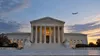 The U.S. Supreme Court building at dusk with a distant passenger aircraft crossing the sky.