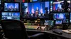 A television broadcast control room displays blurred footage of a government podium on multiple monitors.