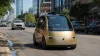 An unbranded gold autonomous taxi traveling on a sunlit downtown Austin street