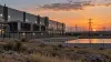 Illustrative Texas data center at dusk beside cooling equipment, transmission lines and a water basin.