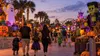 Families walk through a colorful, block-themed Halloween festival at a Florida amusement park at twilight.