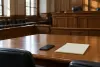 An empty courtroom with an unbranded smartphone and blank legal pad on a counsel table.