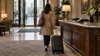 An anonymous traveler rolls a suitcase through an unbranded British hotel lobby on a rainy day.