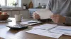 Adult reviews a plain envelope beside a calculator and household bills at a kitchen table