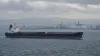 An unbranded oil tanker passes an industrial port under an overcast sky.
