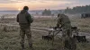 Two unmarked service members prepare a reconnaissance drone at a field exercise at dawn.