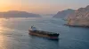 A commercial oil tanker transits calm water between the rugged arid coastlines of the Strait of Hormuz at dawn.