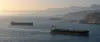 Commercial oil tankers travel through the Strait of Hormuz in subdued morning light.