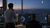 Two space-operations analysts review Earth-to-moon orbital paths in an unbranded control room.