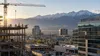 An unbranded Utah employment scene at dawn with commercial construction, modern offices, distant workers and the Wasatch Mountains in the background.