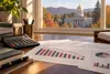Editorial illustration of Vermont budget charts and a calculator on a desk with a gold-domed statehouse in the distance.
