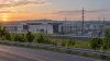 Illustration of a modern Virginia data center campus and electrical substation viewed from a roadside at dawn