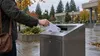 An anonymous voter places a sealed ballot envelope into a drop box in a Pacific Northwest civic plaza.