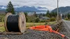 Fiber-optic cable and conduit beside a rural Washington road with homes, forest and mountains.