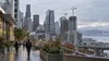 A Pacific Northwest downtown business district with office buildings, construction cranes and distant commuters under overcast skies.
