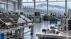 Illustrative Pacific Northwest aerospace workshop with generic satellite components and evergreen hills visible beyond high windows.
