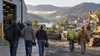 Workers walk near a generic manufacturing facility and construction yard in a wooded Appalachian river valley.