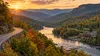 A scenic road winds through an Appalachian mountain valley near a riverside lodge in early autumn light.