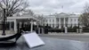 A blank press credential rests near a White House security entrance in a symbolic editorial image.