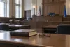 An empty courtroom with a closed law book and reading glasses on a counsel table