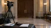 A television camera, two notebooks and an audio recorder positioned outside closed wooden doors in a civic building.
