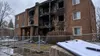 Fire-damaged brick apartment building behind safety fencing with an inspection clipboard in the foreground.