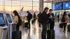 Travelers use digital kiosks and receive staff assistance in a modern airport terminal at sunrise.