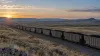 A generic coal train crossing Wyoming high plains at sunrise.